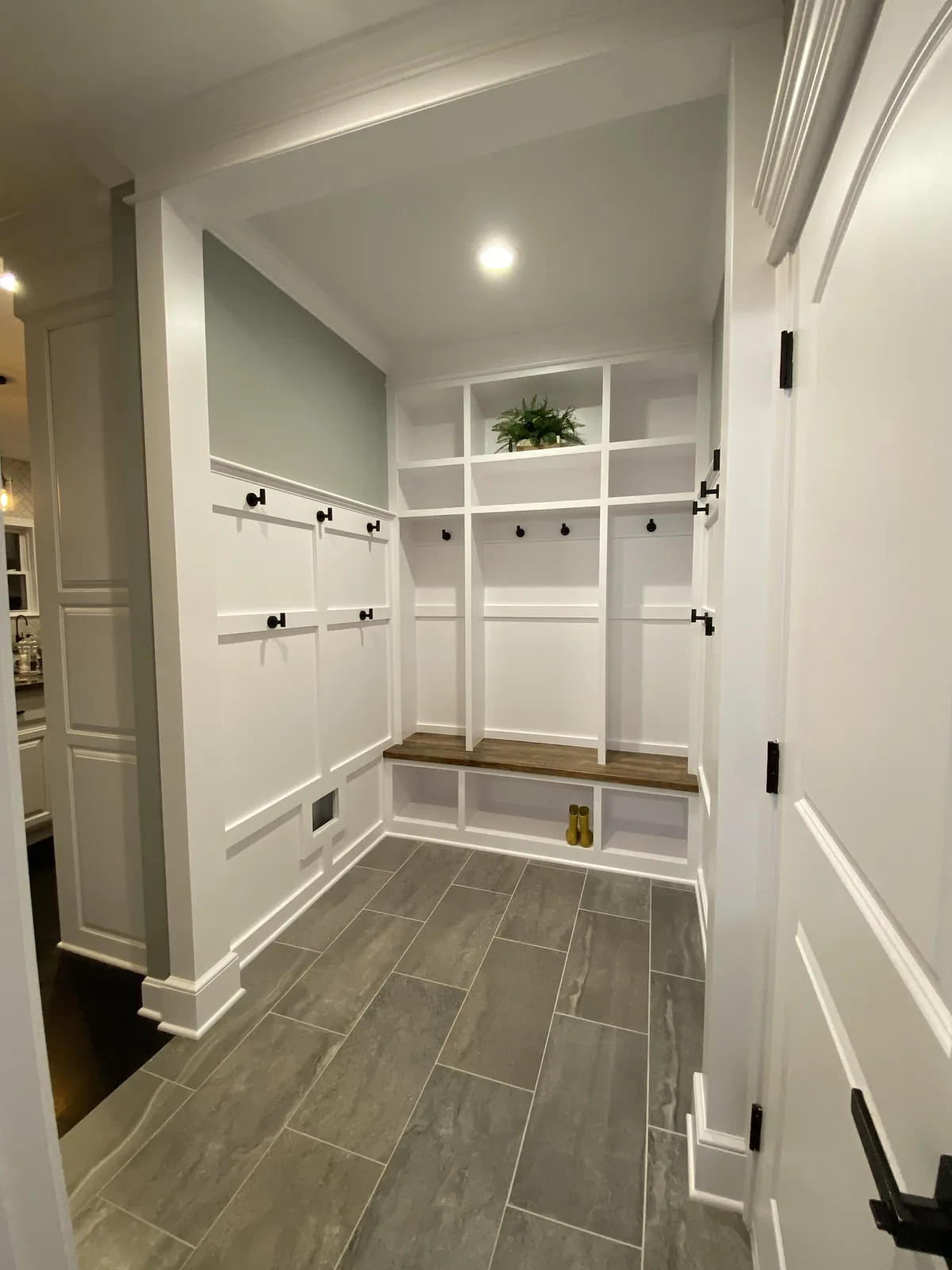 Mudroom remodel in Kansas City, MO with white built-in lockers, black hooks, a walnut bench top, and panelled walls