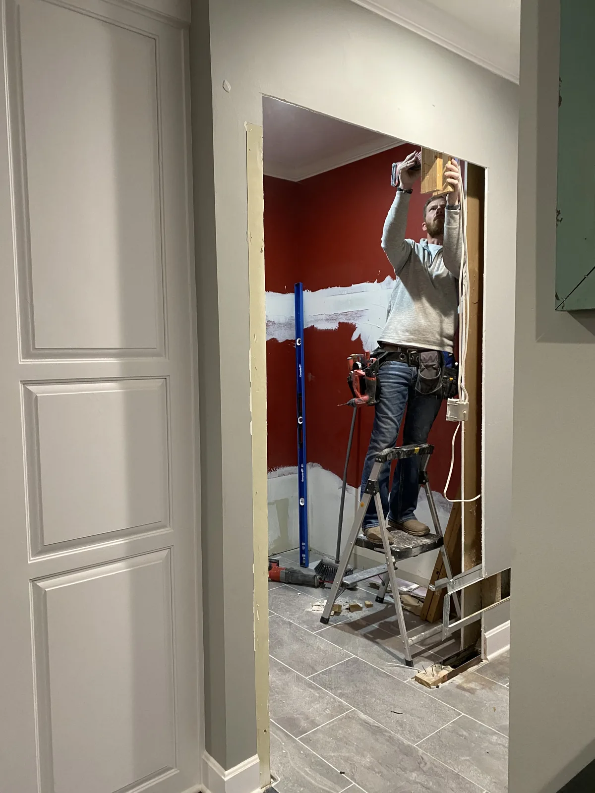 Mudroom remodel in Kansas City, MO in progress: a carpenter on a stepladder working at the head of the new opening, with the original red wall behind