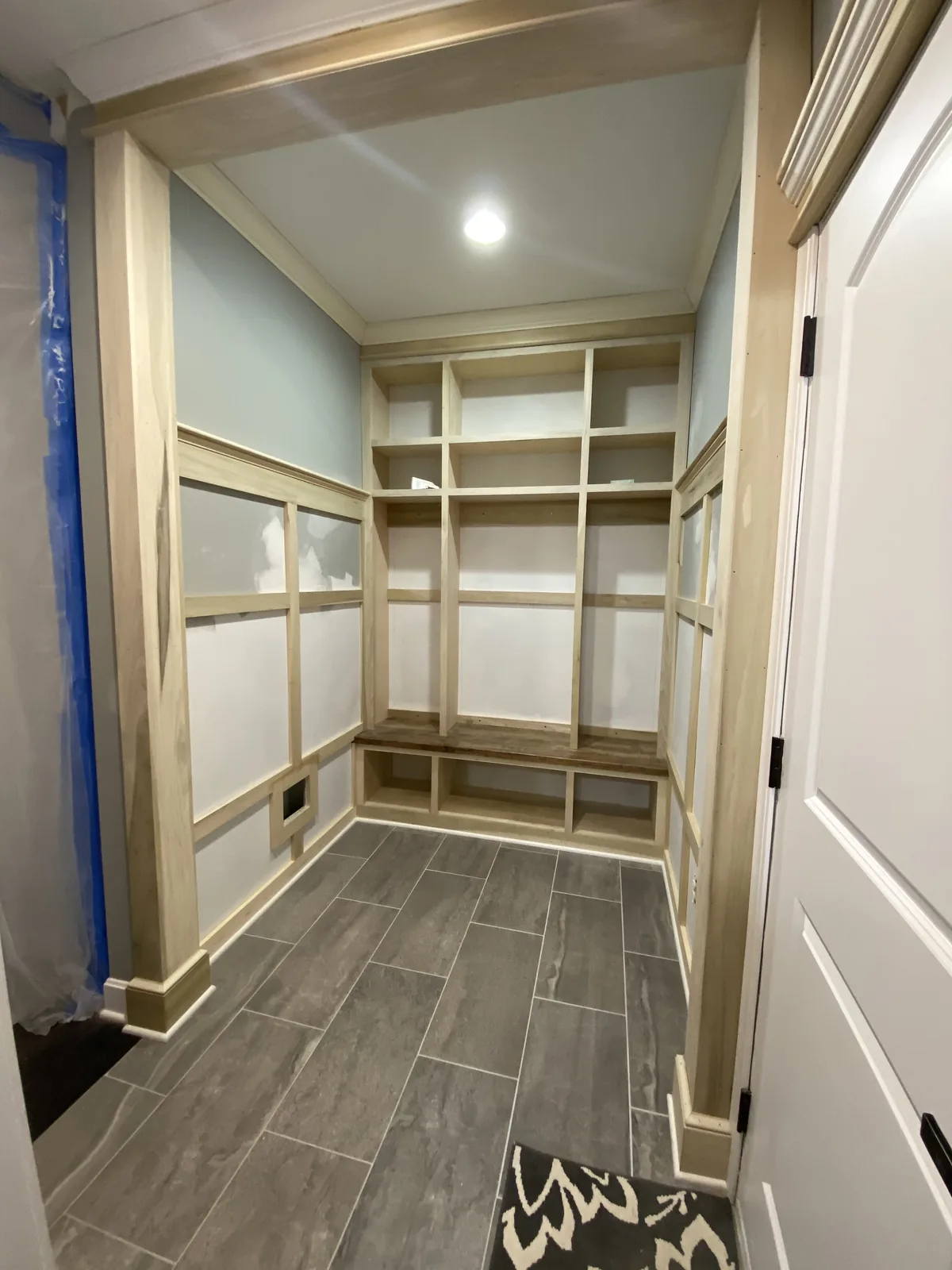 Mudroom remodel in Kansas City, MO before paint: built-in lockers, bench and wall panelling in raw wood, with crown moulding running through a flush ceiling