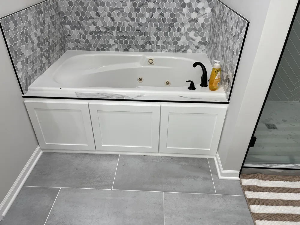 Whole-home remodel in North Kansas City, MO — whirlpool tub with hexagon mosaic surround and custom cabinet apron