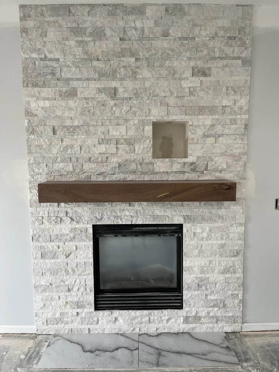 Whole-home remodel in North Kansas City, MO — custom fireplace wall under construction with ledge stone tile and live-edge wood mantel